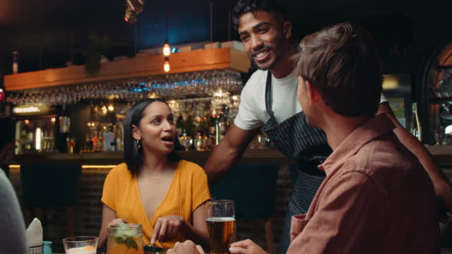 diverse group of friends being served y waiter in restaurant