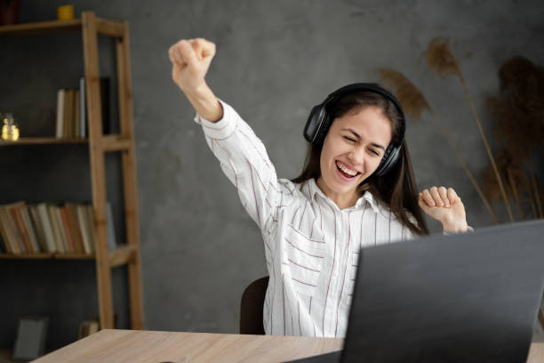 istock Hispanic smiling joyful woman using laptop and wireless headphones while dancing in cozy home indoors 1404796384