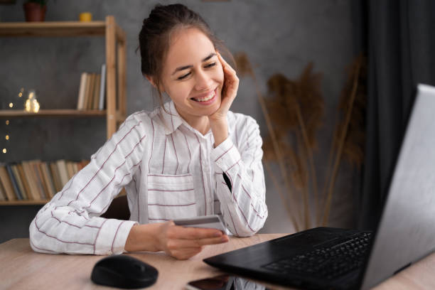 istock Young brunette woman holding credit card and using laptop computer working at home. Businesswoman making online shopping, e-commerce, internet banking, making online payment from home 1404796388