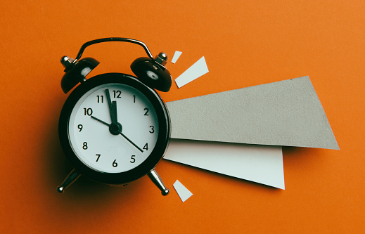 Alarm clock and papers on orange background.