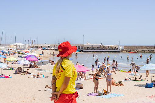 Sitges, Spain - June 12, 2022: Lifeguard in working clothes guarding the beach in Sitges (Spain), selective approach to the yellow shirt.
