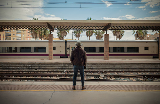 Rear view of adult man on cowboy hat waiting in train station.