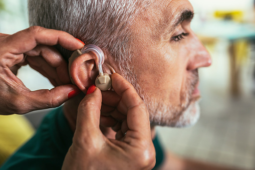 Woman helps mature male patient to use hearing aid.