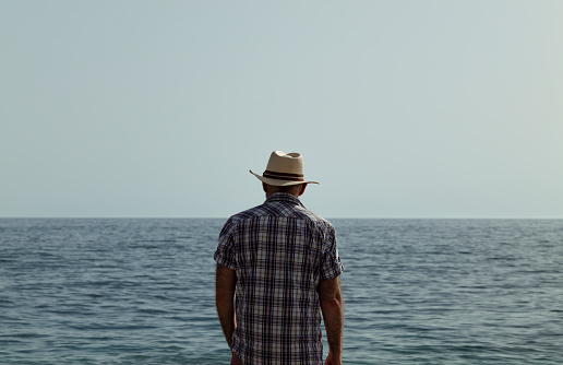 Adult man in hat with open shirt on beach against sea and sky