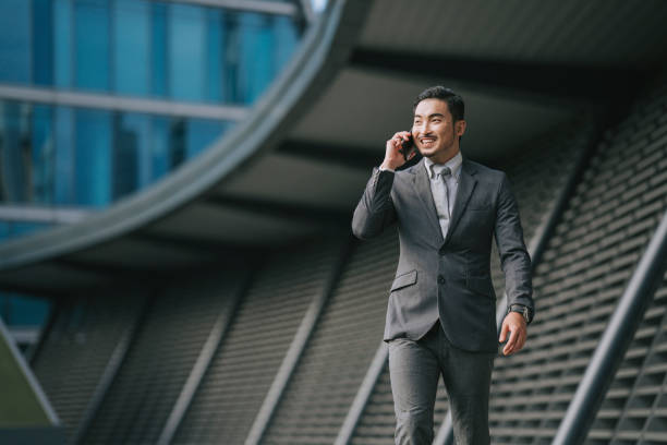 uomo d'affari asiatico cinese di successo che parla attraverso lo smartphone al di fuori dell'edificio finanziario - blazer men suit business foto e immagini stock