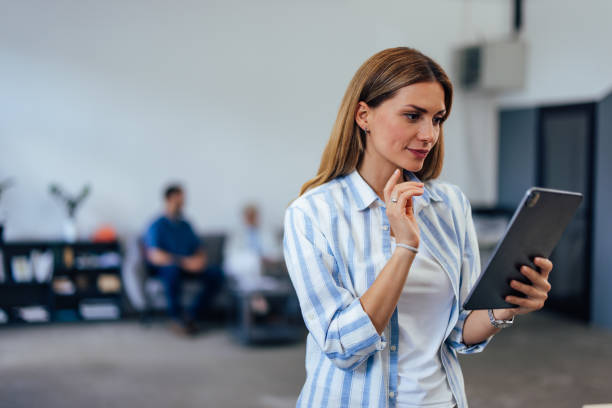 istock Businesswoman looking thoughtful, using a tablet at the office, standing. 1404821377