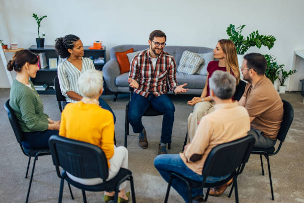 Group of people sitting in a circle talking to each other, having a group therapy appointment. stock photo