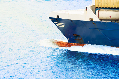 Bow of a large Cargo ship moving through the sea in bright sunlight.