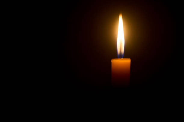 istock A single burning candle flame or light glowing on a yellow candle isolated on red or dark background on table in church for Christmas, funeral or memorial service 1404825849