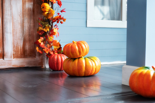 Residential house decorated for Halloween holiday. Different colored pumpkins in front door On Wooden Steps. Porch of yard decorated with orange pumpkins in autumn. Thanksgiving. Halloween outside.