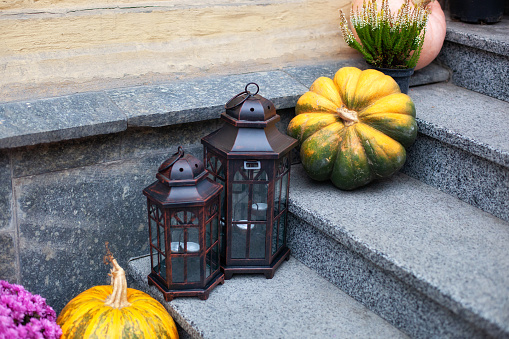 House entrance staircase decorated for autumn holidays, fall flowers and pumpkins. Cozy porch of the house with vintage lanterns in fall time. Halloween design home with yellow pumpkins and lamps
