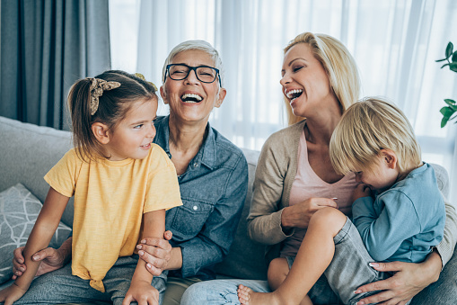 Shot of three generations family relaxing together at home. Cheerful mother and grandmother having fun while playing with their two kids on sofa in the living room.