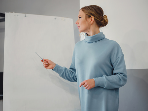 Young female trainer or speaker making whiteboard presentation for employees in office, focused woman trainer presenting business project on flipchart at meeting. mock-up