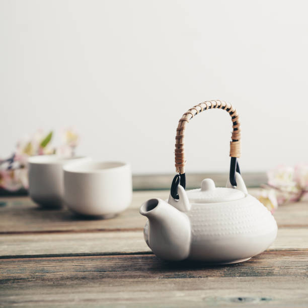 White teapot, cups, sakura flowers on wooden table against the white wall stock photo