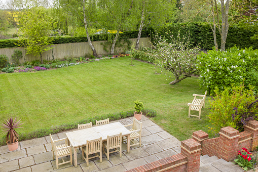 Garden patio with furniture on a terrace in a UK landscaped back garden with large lawn