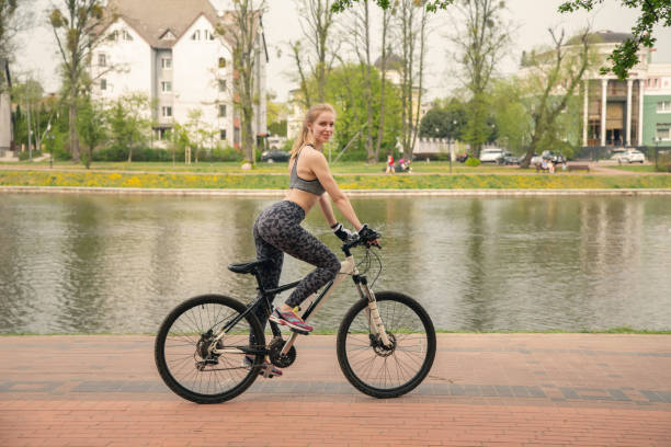 happy blond woman driving on bike in city park near pond