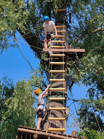 Two teenagers are climbing a rope ladder in a summer rope amusement park.Bottom view