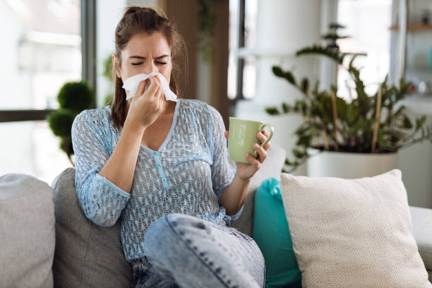 Young woman  blowing nose with a napkin Young woman blowing her nose with a tissue at home cold virus stock pictures, royalty-free photos & images