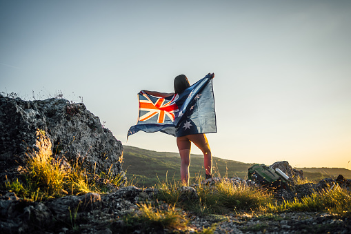 Young woman with flag of Australia on the mountain during sunset