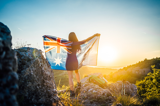 Young woman with flag of Australia on the mountain during sunset