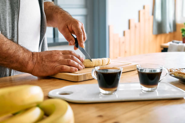 Man making healthy breakfast or brunch, cutting banana for putting it on puffed corn cakes with spread peanut butter. Protein diet healthy eating concept.