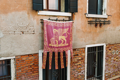 Venice, Italy - July 19, 2017: Hanging flag featuring the winged lion of St. Mark. Winged lions, visible throughout Venice, are the emblem of Saint Mark the Evangelist, patron saint of the city.