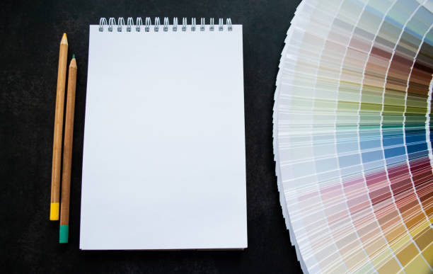 istock Fan paint samples interior design painting. Multicolored natural colors. Black background, white notebook for copy space and pencils 1404850168