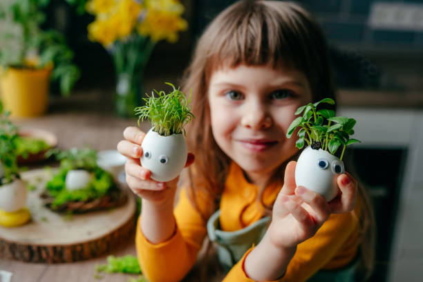 kleines mädchen, das eierschale mit spielzeugaugen auf dem tisch schmückt - craft eggs easter animal egg stock-fotos und bilder