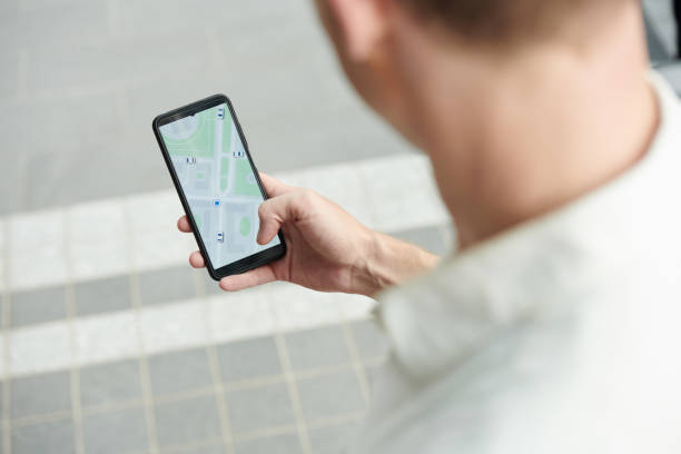 Young man tracking taxi car via application on smartphone, view over shoulder