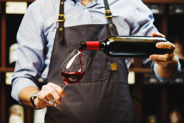 male sommelier pouring red wine into long-stemmed wineglasses. - wijn stockfoto's en -beelden