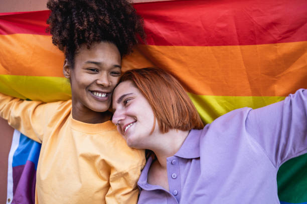 Happy gay couple celebrating pride holding rainbow flag outdoor - LGBTQ and love concept stock photo