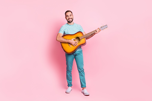 Full length body size view of attractive cheerful guy playing string guitar country isolated over pink pastel color background.
