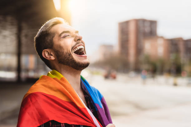 hombre gay feliz divirtiéndose sosteniendo el símbolo de la bandera del arco iris de la comunidad lgbtq - gay pride flag gay pride gay man homosexual fotografías e imágenes de stock