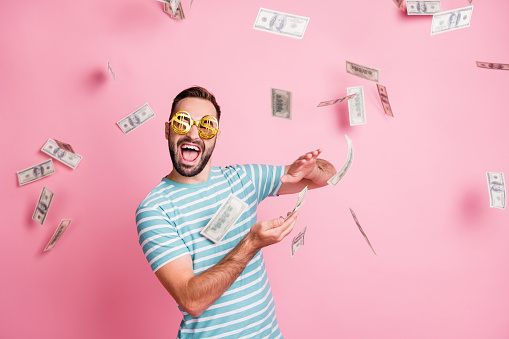 Portrait of nice funky cheerful guy wear dollar specs throwing currency us 100 hundred budget isolated over pink pastel color background.