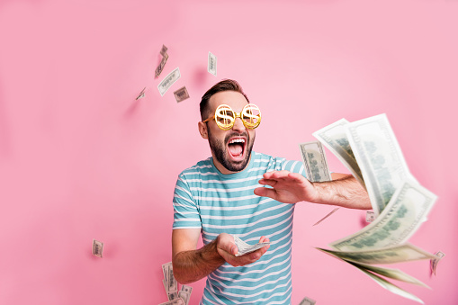 Portrait of nice crazy cheerful guy wear dollar specs throwing us 100 rate budget salary isolated over pink pastel color background.