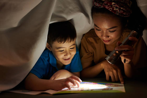 Mother Reading Scary Story for Son Mother shining flashlight on book page when son reading scary story parent and child reading stock pictures, royalty-free photos & images