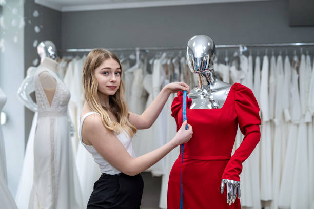 woman saleswoman measures evening dress with tape measure in the salon young charming woman saleswoman measures evening dress with a tape measure in the salon clothing design studio stock pictures, royalty-free photos & images