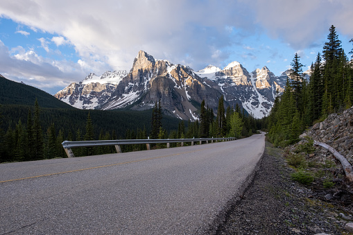 A scenic road with no vehicles and a blue sky with some clouds and snow capped mountains. Clear road through Banff National Park, Canada