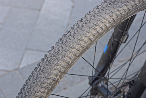 part of a wheel made of gray black rubber tire and metal spokes on a bike in the street