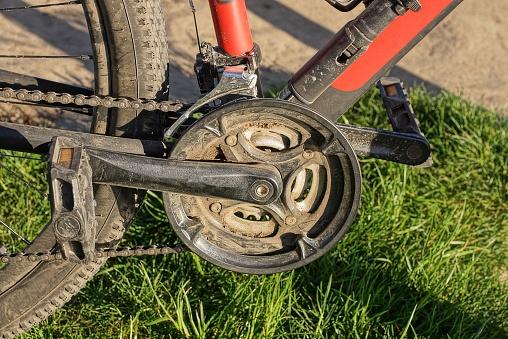 black bicycle pedal on a metal sprocket with a chain on a sports bike in green grass on the street