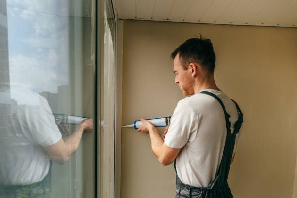 istock Young man wearing overalls sealing cracks between window and trim 1404866732