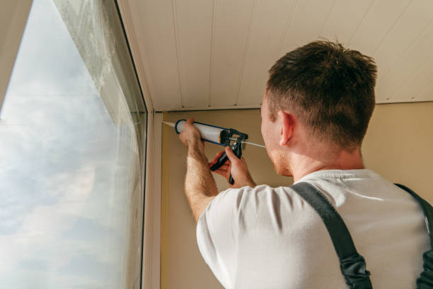 istock Young man wearing overalls sealing cracks between window and trim 1404866755