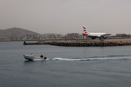 Gibraltar - 16th June, 2022: British Airways aircraft taxis on the Gibraltar airstrip that protrudes into the sea as a boat passes by. Gibraltar is a British Overseas Territory