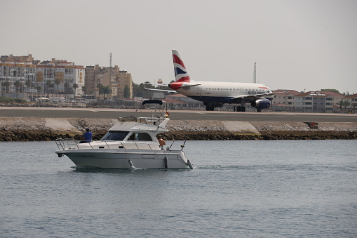 Gibraltar - 16th June, 2022: British Airways aircraft taxis on the Gibraltar airstrip that protrudes into the sea as a boat passes by. Gibraltar is a British Overseas Territory