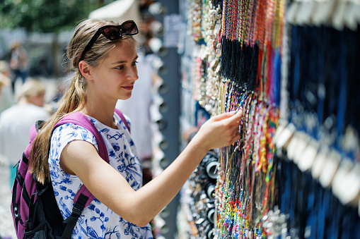 Happy teenage girl browsing necklaces on a jewelry street market stand.\nCanon R5
