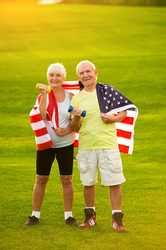 Couple wrapped in American flag. Senior people holding dumbbells. Strength and pride of citizens. New victories await.