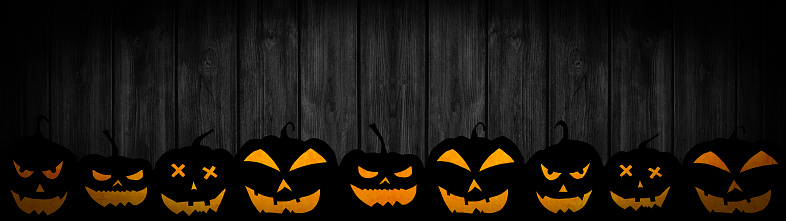 HALLOWEEN background banner wide panoramic panorama template -Silhouette of scary carved luminous cartoon pumpkins, isolated on dark black wooden boards wood wall texture