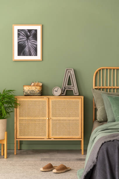 istock Stylish composition of modern bedroom interior. Mock up poster frame, rattan commode, beautiful bedclothes and creative personal accessories. Sgae green wall. Template. Copy space. 1404874602