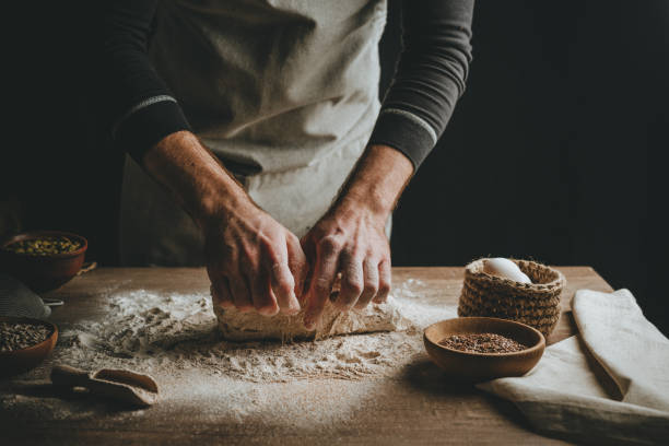 istock Young man kneading dough on dark background. 1404874855