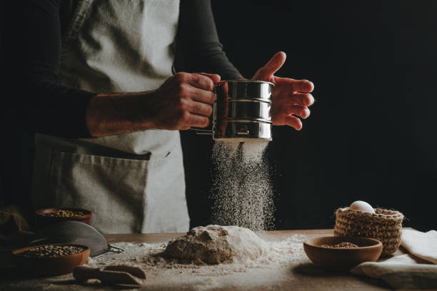istock Young man kneading dough on dark background. 1404874866